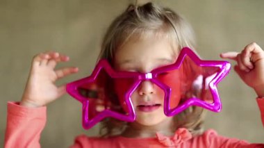 Büyük pembe gözlüklü, yıldız şeklinde komik küçük kız kameraya bakıyor. Pembe gözlüklü güzel kız kameraya bakıyor. Gözlüklü kız