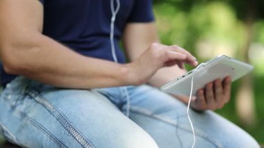 Adam tablet bilgisayarındaki fotoğraflara bakıyor. Beyaz tablet tabletli ve kulaklıklı erkek elleri. Adam beyaz tablet tableti tutuyor. Adam bakar ve bilgisayarındaki fotoğraflara bakar.