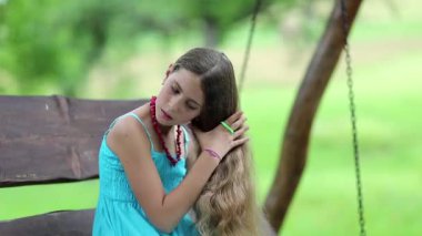 Güzel kız onun uzun saçlarını tarıyor. Mavi elbiseli çekici kız bankta oturur ve uzun saçlarını tarar.