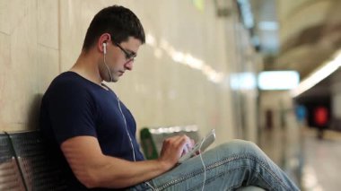 Tablet bilgisayarı olan adam yeraltı istasyonundaki bankta oturuyor. Adam metro istasyonundaki metal bankta oturuyor ve tablet bilgisayar kullanıyor. Tablet bilgisayarlı bir iş adamı. Tablet bilgisayarlı erkek