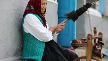 Yaşlı kadın bankta oturur ve dönen tekerlekle distaff üzerinde çalışır. Ukraynalı yaşlı kadın evinin yanındaki bankta oturur ve iplik örer. Dönen tekerli bir kadın, el işi.