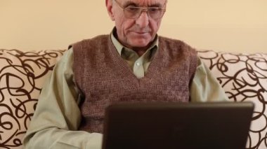 Not defterli yaşlı bir adam. Üst düzey adam dizüstü bilgisayarla mesaj yazar. Kanepede dizüstü bilgisayarlı bir adam.