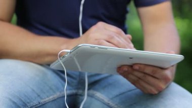 Adam tablet bilgisayarındaki fotoğraflara bakıyor. Adam beyaz tablet tableti tutuyor. Beyaz tablet tabletli ve kulaklıklı erkek elleri. Adam tablet bilgisayardaki fotoğraflara bakar ve bakar.