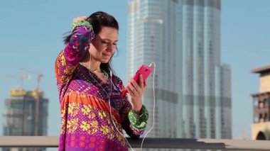 Kadın Megatall gökdelenin yanında duruyor ve akıllı telefon kullanıyor. Akıllı telefonlu bir kadın. İş kadını, akıllı telefonundaki fotoğraflara bakar ve göz gezdirir. Yetişkin kadın akıllı telefon kullanıyor.