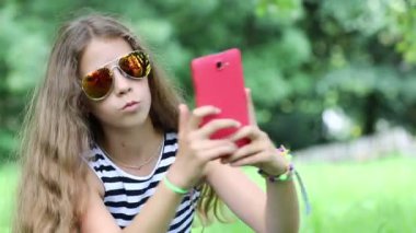 Güneş gözlüklü güzel kız akıllı telefonunda selfie çekiyor. Kırmızı cep telefonlu çekici bir kız fotoğraf çekiyor. Kadın kırmızı akıllı telefondan fotoğraf çekiyor.