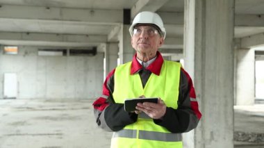 İnşaat alanında Tablet PC ile birlikte beyaz başlıklı usta inşaatçı. İnşaat alanındaki elektronik cihazlarla ilgili çalışmaların yöneticisi. Bina denetimi. Proje alanında beyaz kasklı bir işçi