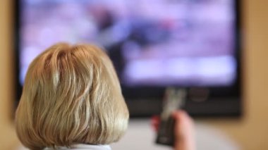 Sarışın kadın uzaktan kumanda ile tv kanalları geçin. Kafanın arkasında. Kadın televizyon