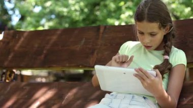 Tabletli güzel kız bahçede salıncakta oturuyor. Tablet bilgisayarında oyun oynayan bir kız. Küçük kız salıncakta oturuyor ve Tablet PC kullanıyor. Tabletli güzel kız.