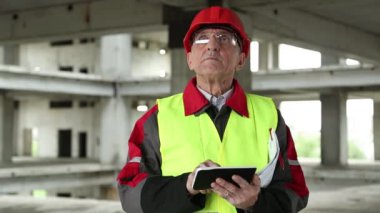İnşaat alanında Tablet PC ile birlikte beyaz başlıklı usta inşaatçı. Bina denetimi. İnşaat alanındaki elektronik cihazlarla ilgili çalışmaların yöneticisi. Proje alanında beyaz kasklı bir işçi