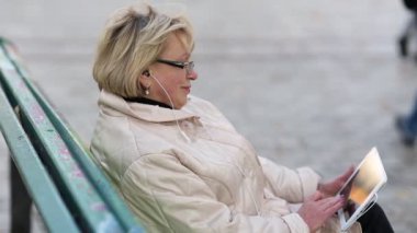 Yaşlı kadın bankta oturuyor ve tablet bilgisayar kullanıyor. Beyaz tablet bilgisayarı olan bir kadın. Tablet bilgisayarı olan bir kadın. Tablet Bilgisayarlı İş Kadını