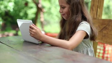 Masada beyaz tabletli güzel bir kız oturuyor. Kız oyunu onun tabletinde oynuyor. Tabletli küçük kız bahçede bankta oturuyor. Tablet bilgisayarı olan kadın