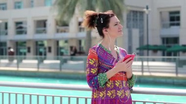 Kadın kırmızı akıllı telefon ve kulaklık ile müzik dinliyor. İş kadını ile smartphone. Erkek smartphone ile suyun kenarında duruyor ve müzik dinliyor. Yetişkin kadın smartphone ile earpieces kullanır.