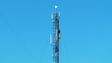 Üç işçi bir baz istasyonunu tamir ediyor. Yüksek irtifa işi. İşteki işçiler. Yeni kablolar döşeniyor. Mavi arkaplandaki baz istasyonu