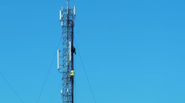 Tamirciler baz istasyonuna hizmet ediyor, yeni ekipmanlar kuruyor. Yüksek irtifa işi. Mavi arkaplandaki baz istasyonu