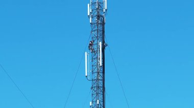 Yüksek irtifa işi. İki işçi baz istasyonuna hizmet ediyor, yeni ekipmanlar kuruyor. Mavi arkaplandaki hücre kulesi, eğim görüntüsü