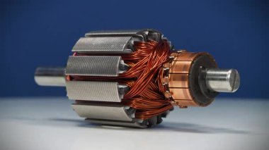 Küçük bir ev aletinin bakır bobinli elektrikli motoru, mavi arka planda dönüyor.