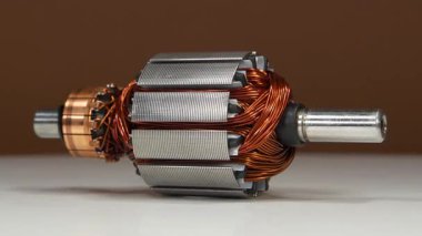 Elektrikli bir motorun armatür veya rotoru, küçük bir ev aletinin bakır bobini, yani perküsyon masajcısı, kahverengi arka planda döner.