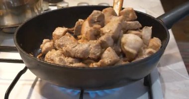 Aşçı et parçalarını gaz sobasında kızartma tavasında karıştırır. Kızarmış et. Sonra, aşçı tavayı gaz sobasından çıkardı.