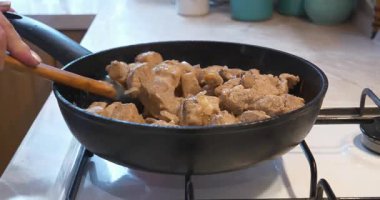 Kızarmış et. Aşçı, et parçalarını soğanla karıştırıyor. Gaz ocağında kızartma tavasında.