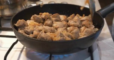 Kızarmış et. Aşçı, et parçalarını soğanla karıştırıp, gaz sobasında kızartma tavasına koyar.