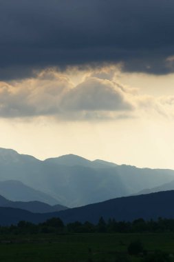 Güneş, Hırvatistan 'ın Velebit dağlarının çizilmiş siluetleriyle bulutların arasında parlıyor