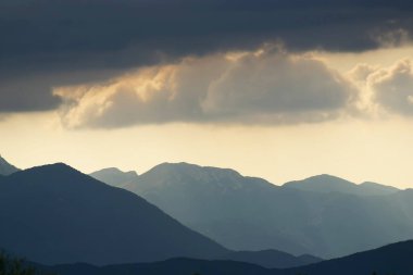 Güneş, Hırvatistan 'ın Velebit dağlarının çizilmiş siluetleriyle bulutların arasında parlıyor