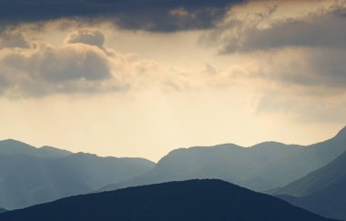 Güneş, Hırvatistan 'ın Velebit dağlarının çizilmiş siluetleriyle bulutların arasında parlıyor