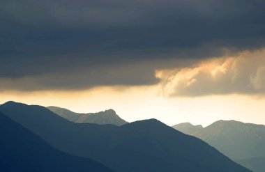 Güneş, Hırvatistan 'ın Velebit dağlarının çizilmiş siluetleriyle bulutların arasında parlıyor