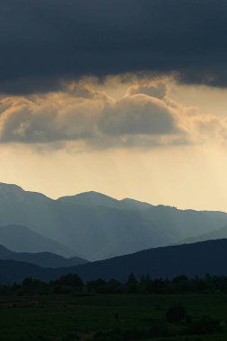 Güneş, Hırvatistan 'ın Velebit dağlarının çizilmiş siluetleriyle bulutların arasında parlıyor