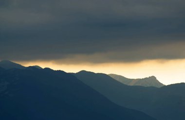 Güneş, Hırvatistan 'ın Velebit dağlarının çizilmiş siluetleriyle bulutların arasında parlıyor