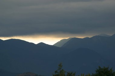 Güneş, Hırvatistan 'ın Velebit dağlarının çizilmiş siluetleriyle bulutların arasında parlıyor