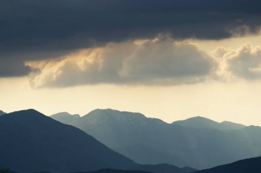 Güneş, Hırvatistan 'ın Velebit dağlarının çizilmiş siluetleriyle bulutların arasında parlıyor
