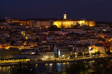 Geceleri hareketli bir şehir manzarası, yoğun nüfuslu bir bölgenin üzerinde şehir ışıklarını yansıtan dolambaçlı bir nehirle aydınlatılmış bir tepe kalesini gözler önüne seriyor..