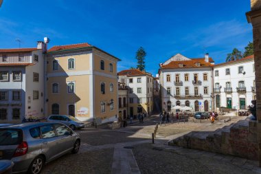 Avrupa şehir meydanında güneşli bir günde geleneksel mimarisi, kaldırım taşı meydanı ve park edilmiş arabaları olan renkli binalar canlı bir şehir manzarası yakalıyor..