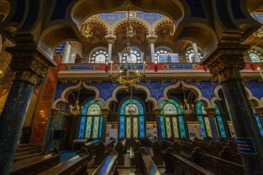 Süslü bir kemer yolu, altın bir avize, vitraylı pencereler ve yumuşak ışıklandırma, Kudüs sinagogu ve Kudüs sinagogu tarafından aydınlatılmış ahşap sıralar içeren detaylı bir iç görünüş.