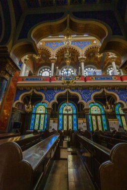 Süslü bir kemer yolu, altın bir avize, vitraylı pencereler ve yumuşak ışıklandırma, Kudüs sinagogu ve Kudüs sinagogu tarafından aydınlatılmış ahşap sıralar içeren detaylı bir iç görünüş.