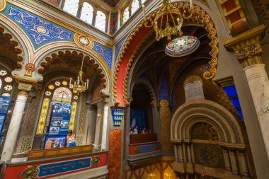 Bir sinagogun canlı bir iç görüntüsü süslü bir balkon, kemerli açıklıklar, karmaşık duvar tasarımları ve yüksek pencerelerden gelen yumuşak ışıkla yıkanmış avizeler, Kudüs sinagogu.