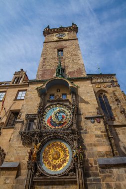 Avrupa 'da tarihi bir kilisenin bulunduğu geniş bir kaldırım taşı meydanı. Çarpıcı kuleler, renkli cepheli binalar, göze çarpan bir anıt ve parçalı bulutlu bir gökyüzü altında güneşli günün keyfini çıkaran çok sayıda insan..