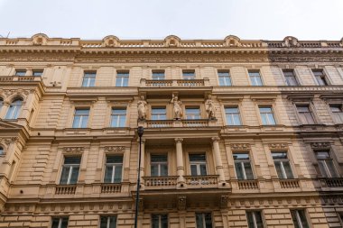 Dekoratif pervazlar, sıra sıra pencereler ve heykellerle dolu merkezi bir balkonun yer aldığı çok katlı tarihi bir bina açık gökyüzüne karşı duruyor..
