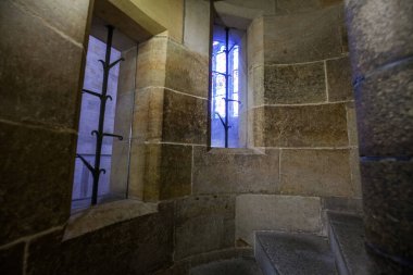 İki küçük pencereli taştan sarmal bir merdivenin yakın çekim görüntüsü. Bir tanesinde mavi cam belirtiler var..