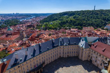 Geniş bir Avrupa şehrine ev sahipliği yapan yüksek açılı bir şehir, kırmızı kiremitli çatıları olan, yüksek bir noktadan görünen, ön planda bir taş balyoz, açık mavi bir gökyüzü altında.