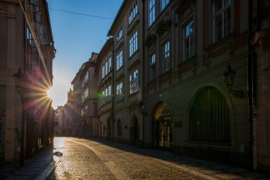 Tarihi binalarla dolu dar bir kaldırım taşı caddesi, kemerli kapı ve pencerelerle kaplı, yıldız patlaması etkisi ile sıcak güneş ışığıyla yıkanmış, cadde boyunca uzun gölgeler bırakarak.