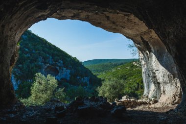 Buracas do Casmilo, a natural formation in Portugal, featuring a rocky cliffside dotted with large caves. These caves are set in a lush landscape with a dirt path winding through olive trees and green foliage. The lighting highlights the textures of  clipart