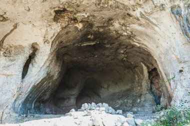 Buracas do Casmilo, a natural formation in Portugal, featuring a rocky cliffside dotted with large caves. These caves are set in a lush landscape with a dirt path winding through olive trees and green foliage. The lighting highlights the textures of  clipart