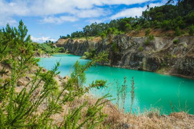 Kıyı şeridi boyunca dar bir yolu olan kayalık kayalıklar ve yemyeşil bitki örtüsüyle çevrili çarpıcı bir turkuaz göl doğanın güzelliğini huzurlu ve manzaralı bir şekilde gösteriyor.