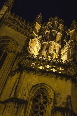 Batalha Manastırı gece aydınlandı. Manastırın görkemli Gotik mimarisi, karmaşık taş işçiliği ve sıcak bir ışıltıyla yıkanmış yüksek kuleleriyle güzelce vurgulanıyor. Kral I. John 'un heykeli, at sırtında duruyor. 