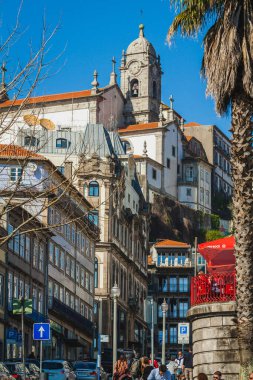 Avrupa 'da tarihi binalarla dolu hareketli bir cadde, bir tepenin üzerine tünemiş, saat kulesi ve canlı şehir manzarasına karşı duran mimari detaylarıyla tanınmış bir kiliseye kadar uzanıyor.