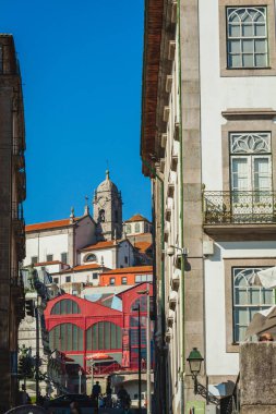 Porto 'nun katmanlı manzarası, geleneksel Portekiz mimarisi tarafından çerçevelenmiş canlı bir kırmızı pazar binası ve arka planda tepe üzerine tünemiş bir kilise. Kompozisyon, şehrin eski ve yeni karışımını renkli modern elementlerle vurguluyor.
