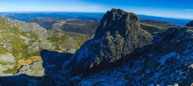 Uçsuz bucaksız vadilere tepeden bakan kayalık bir tepenin panoramik görüntüsü ve berrak mavi gökyüzünün altındaki uzak tepeler engebeli manzaranın muazzam güzelliğini ve ölçeğini yansıtıyor.