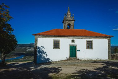 Bina beyazlatılmış duvarlar, yeşil kapılar ve pencereler ve yukarıdaki açık mavi ile güzel zıtlaşan çarpıcı kırmızı kiremitli bir çatıya sahiptir.